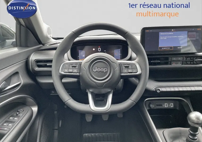 Intérieur du Jeep Avenger 2024 blanc neige, vue frontale sur le volant, tableau de bord numérique et levier de vitesse manuel.
