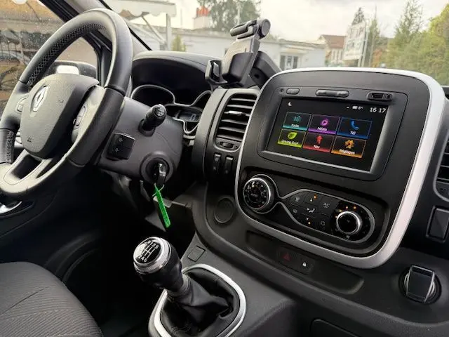 Vue intérieure côté conducteur du Renault Trafic Fourgon gris platine, mettant en valeur le tableau de bord avec écran tactile et levier de vitesses manuel.