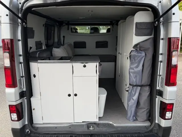 Vue arrière ouverte du Renault Trafic Fourgon gris platine aménagé avec kitchenette et rangements intégrés.