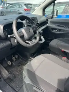Intérieur côté conducteur du Citroën Berlingo XL blanc, vue sur volant, tableau de bord et sièges tissu noirs.