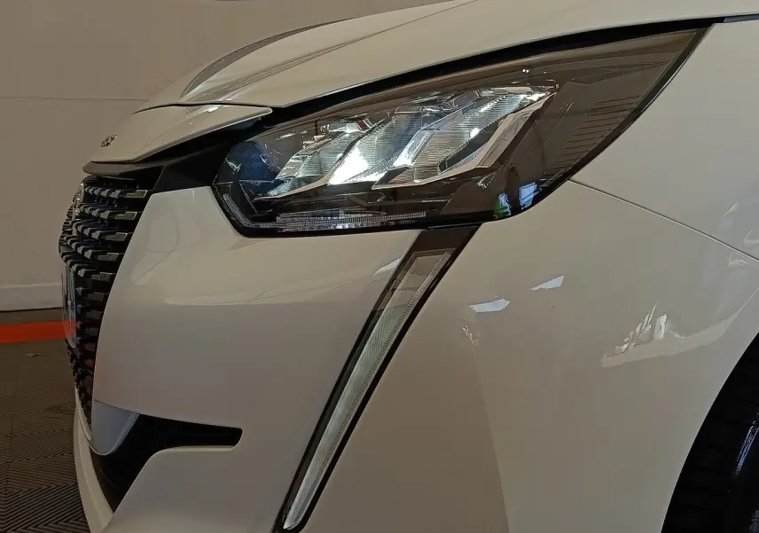 Gros plan sur l'avant droit blanc d'une Peugeot 208 2023, mettant en valeur le phare LED et la calandre noire.