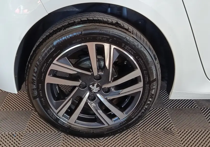 Gros plan sur la roue avant droite d'une Peugeot 208 blanche, avec jante alliage bicolore et pneu Michelin.