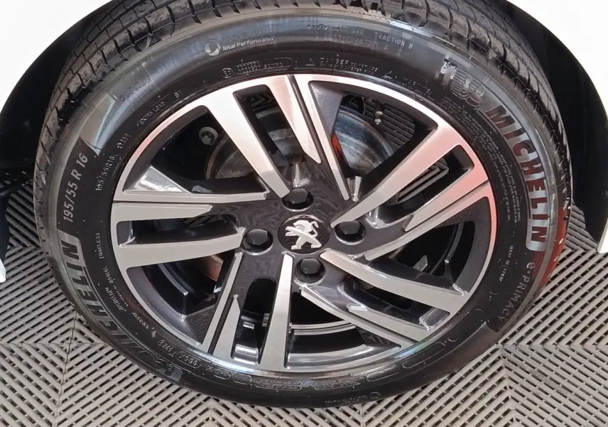 Gros plan sur la jante alliage bicolore avec logo Peugeot d'une 208 PureTech blanche, pneu Michelin visible.
