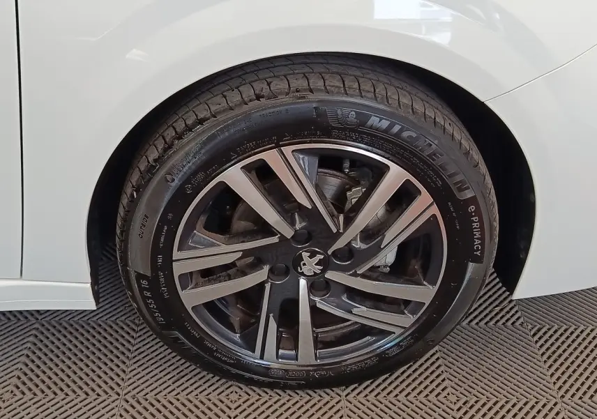 Gros plan sur la roue avant gauche d'une Peugeot 208 blanche, jante alliage au design moderne avec logo lion central.