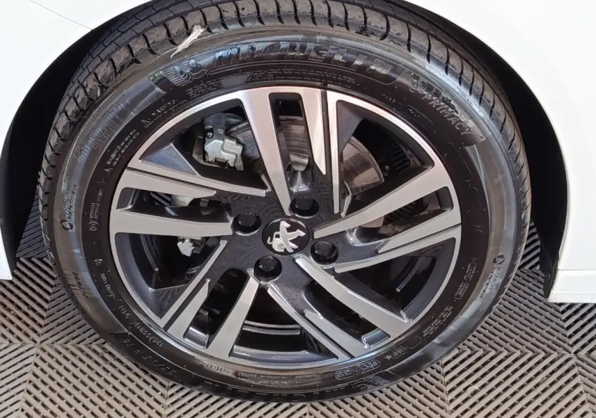 Gros plan sur la roue avant droite de la Peugeot 208 blanche, mettant en valeur la jante alliage noire et argentée au logo lion.