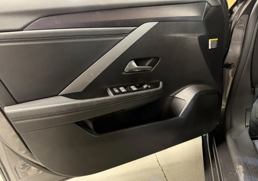 Vue intérieure de la porte avant gauche grise de l'Opel Astra 2024 avec commandes de vitres et accoudoir en cuir noir.