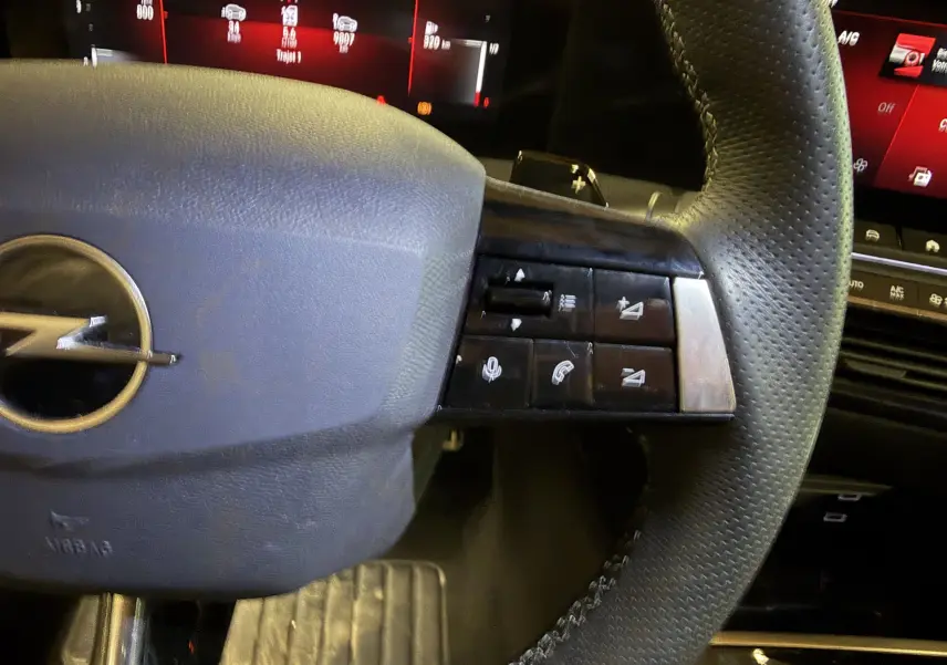 Gros plan sur le volant cuir noir de l'Opel Astra 2024 avec commandes multifonctions et palettes au volant.