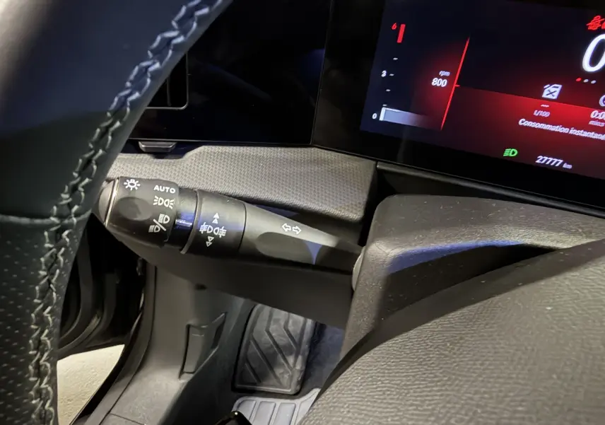 Gros plan sur la commande des phares et clignotants à gauche du volant de l’Opel Astra 2024 gris, tableau de bord numérique visible.