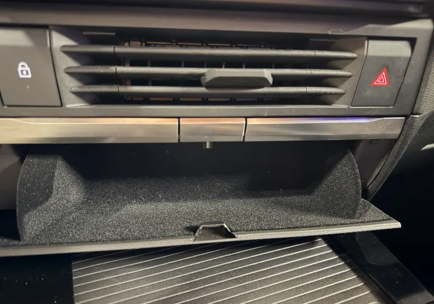 Gros plan sur la boîte à gants ouverte et la ventilation centrale du tableau de bord intérieur noir de l’Opel Astra 2024.