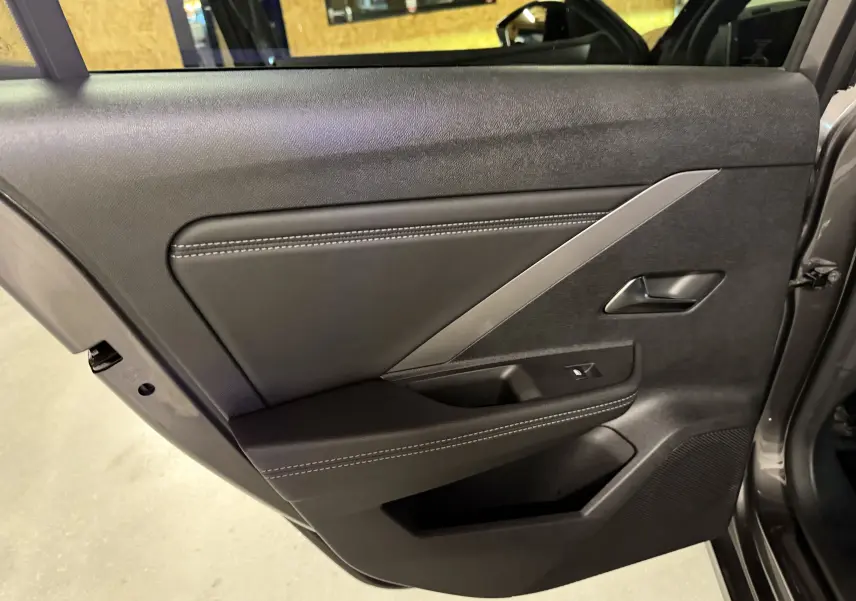 Vue intérieure du panneau de porte arrière gauche de l'Opel Astra gris 2024 avec surpiqûres blanches et insert argenté.