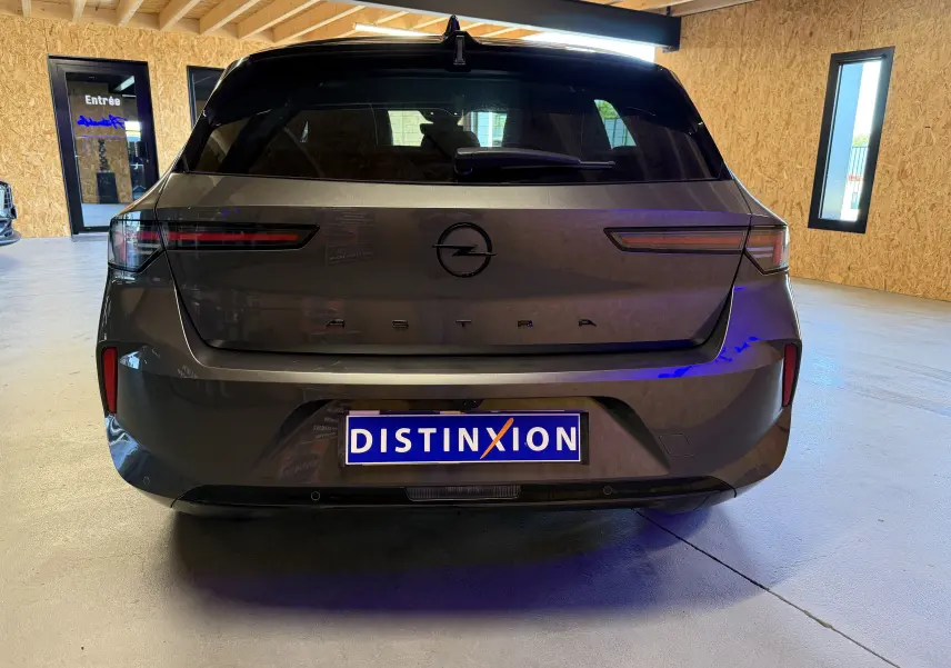 Vue arrière d'une Opel Astra gris métallisé 2024 avec feux LED fins et logo central noir dans un garage.
