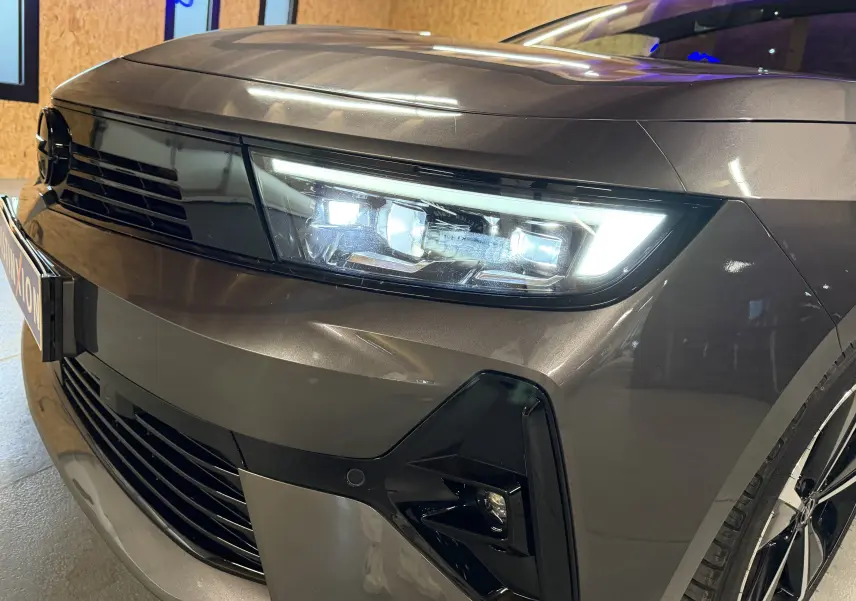 Gros plan sur l'avant droit gris métallisé de l'Opel Astra 2024 avec phares LED allumés et calandre noire brillante.
