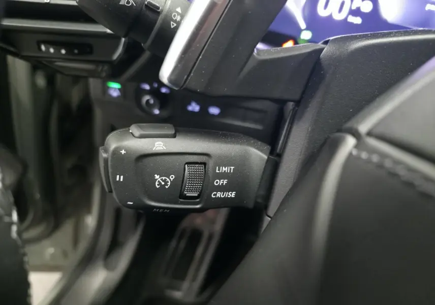 Gros plan sur la commande de régulateur de vitesse au volant du DS7 Crossback gris, avec affichage numérique en arrière-plan.