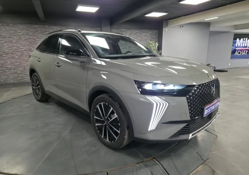 DS7 Crossback gris en 3/4 avant droit, avec calandre noire brillante et feux LED distinctifs allumés.