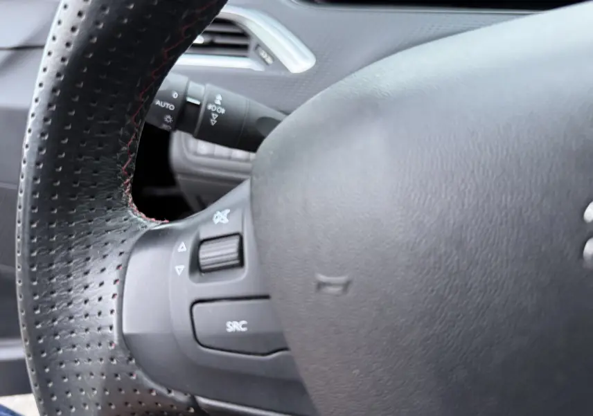 Gros plan sur le volant noir perforé du Peugeot 2008 1.2 PureTech 110 GT Line, avec commandes intégrées visibles.