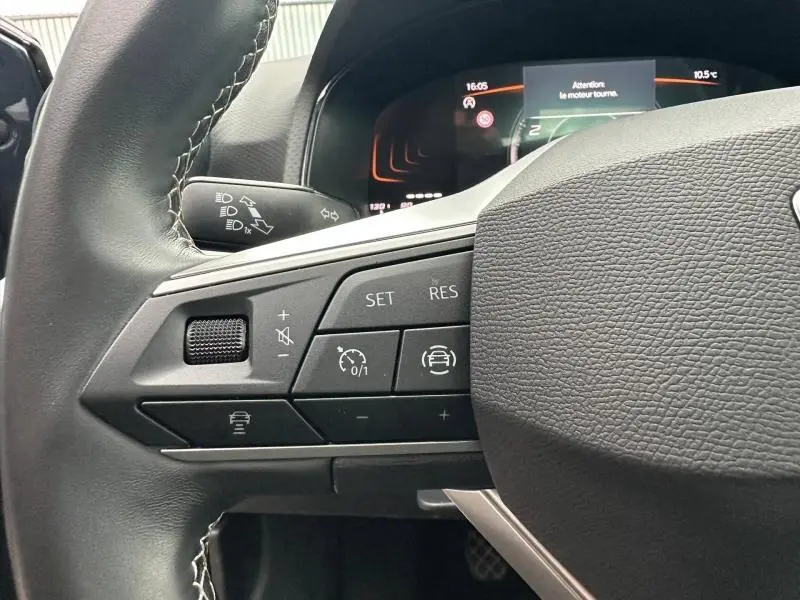 Gros plan sur le volant côté gauche du SEAT Arona 2025 avec commandes de régulateur et tableau de bord numérique en arrière-plan.