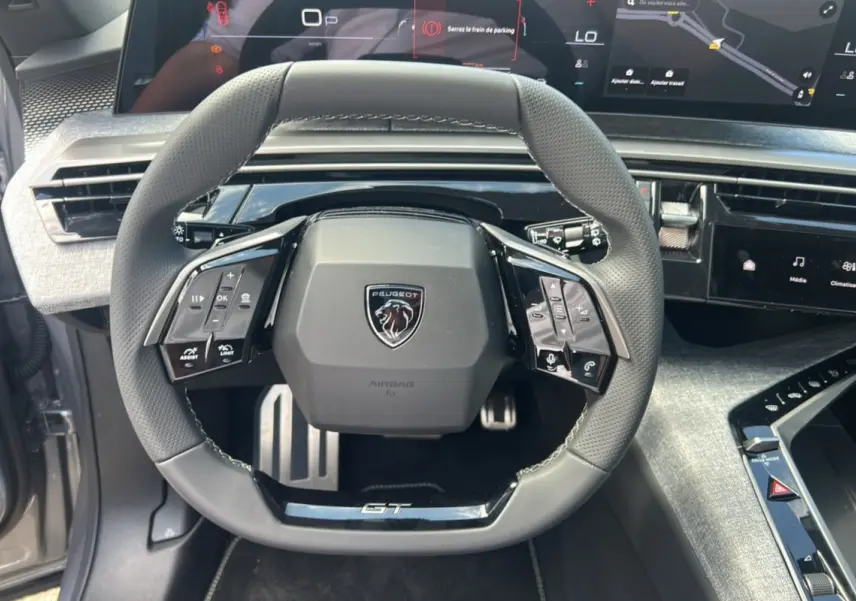 Vue rapprochée du volant cuir multifonctions GT du Peugeot 5008 Hybrid 145 gris Artense avec tableau de bord numérique.
