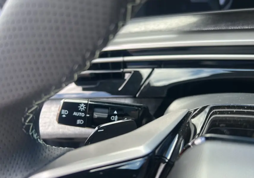 Gros plan sur la commande des feux et clignotants derrière le volant cuir perforé du Peugeot 5008 gris Artense.