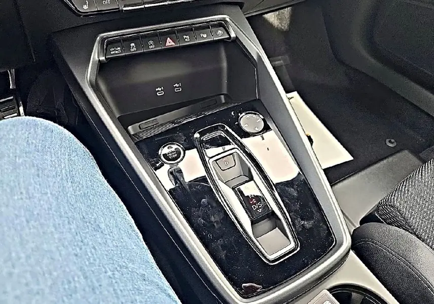 Vue rapprochée de la console centrale noire brillante de l'Audi A3 Sportback 2026 avec sélecteur de boîte auto et boutons multifonctions.
