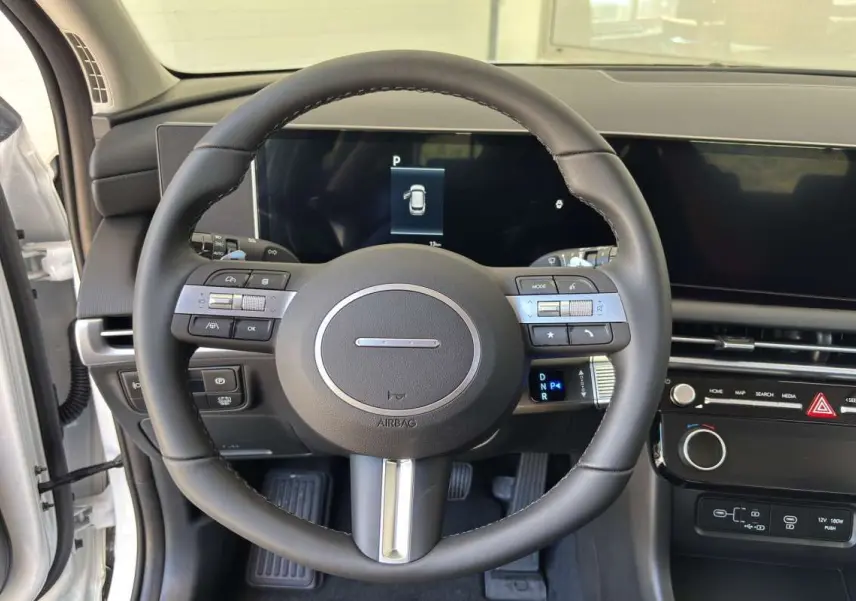Vue intérieure centrée sur le volant cuir multifonctions du Hyundai Tucson blanc atlas, avec tableau de bord digital.