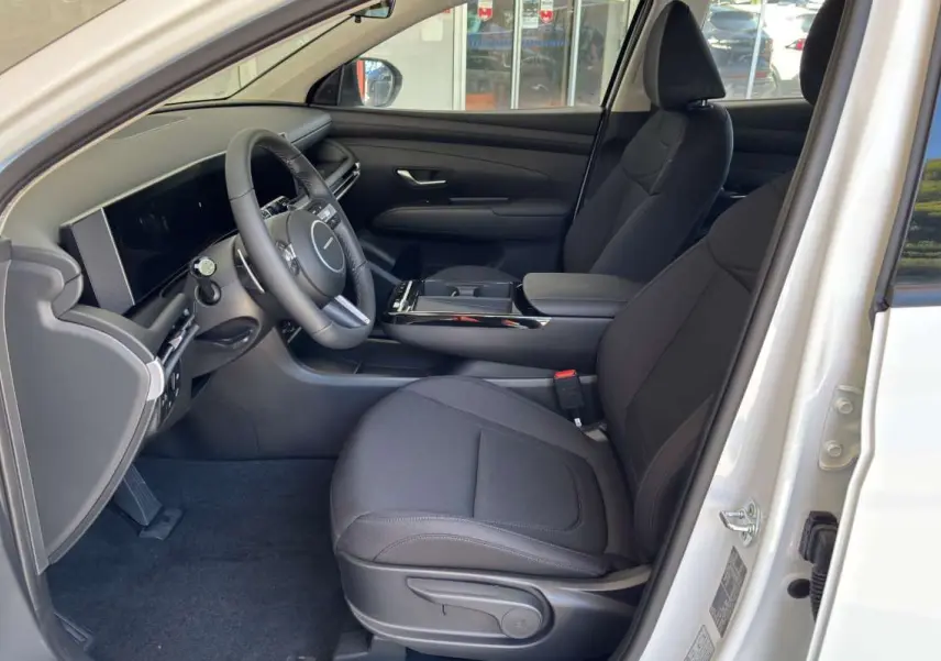 Intérieur côté conducteur du Hyundai Tucson blanc atlas 2026, montrant sièges tissu noirs et tableau de bord moderne.