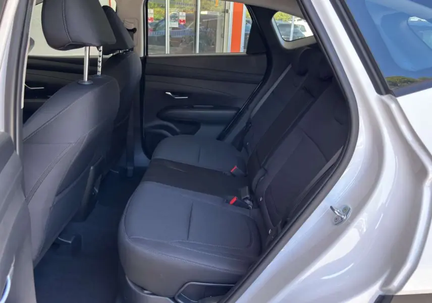 Vue intérieure côté gauche sur la banquette arrière tissu noire du Hyundai Tucson blanc atlas 2026 avec porte ouverte.