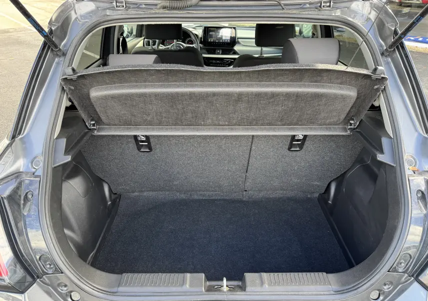 Coffre ouvert vu de l'arrière d'une Suzuki Swift 1.2 Hybrid Privilege gris, avec tablette arrière relevée et intérieur visible.