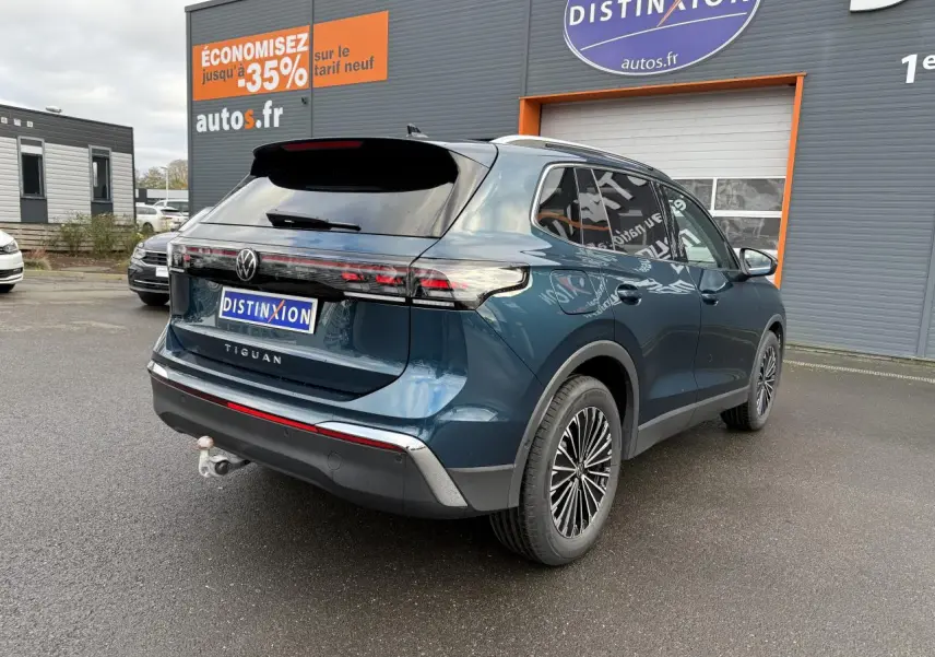 Vue 3/4 arrière droite du Volkswagen Tiguan 2024 bleu métallisé avec crochet d'attelage escamotable et jantes alliage.