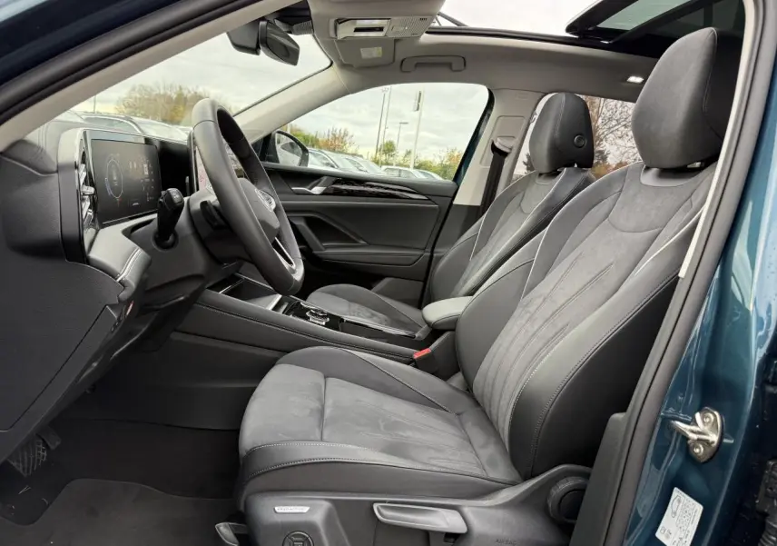 Vue intérieure côté conducteur du Volkswagen Tiguan 2024 bleu Nightshade avec sièges gris et toit ouvrant panoramique.