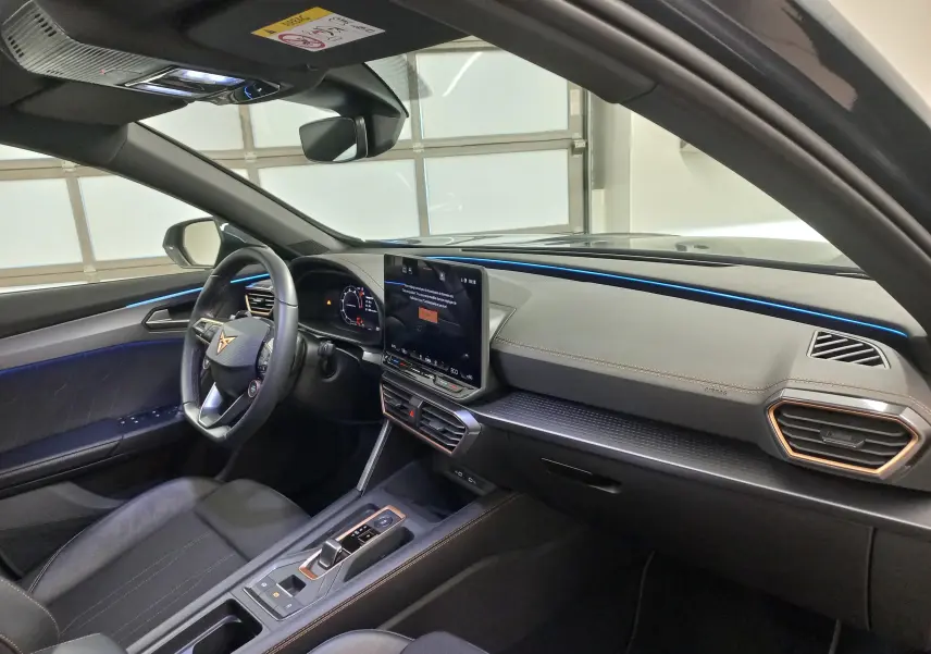 Intérieur de la CUPRA Formentor 1.5 EHybrid 2025 vu côté conducteur, avec éclairage d'ambiance bleu et écran tactile central.
