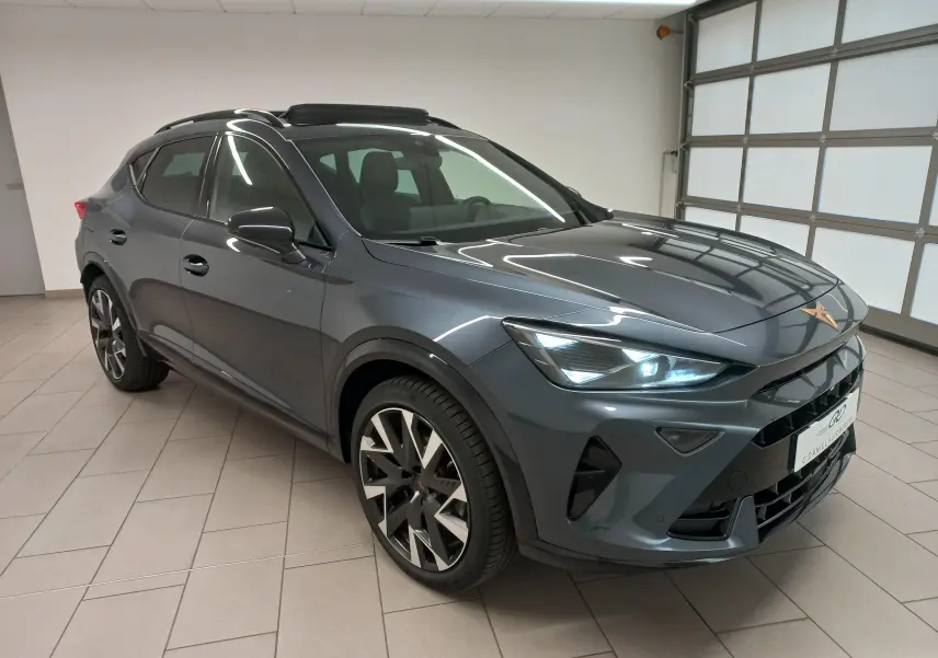 Vue 3/4 avant du CUPRA Formentor gris magnétique 2025 avec toit ouvrant panoramique et phares allumés en intérieur.