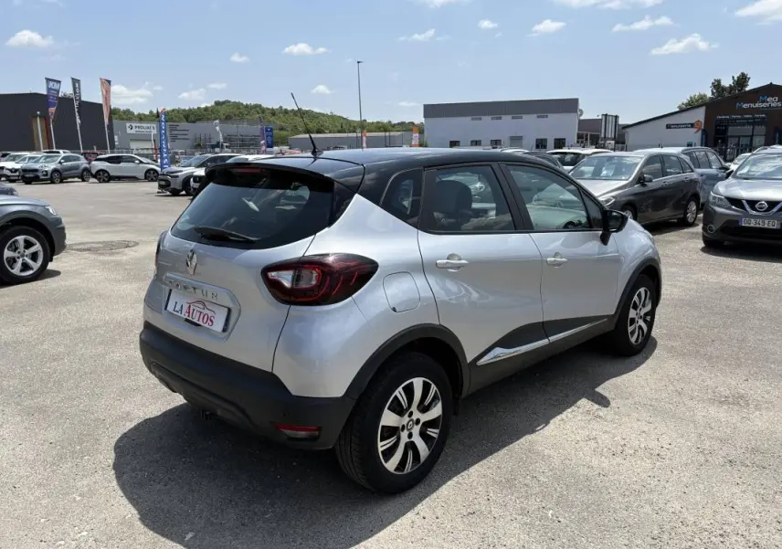 Renault Captur gris vue 3/4 arrière droit, toit noir, jantes aluminium, stationné en extérieur sous ciel clair.