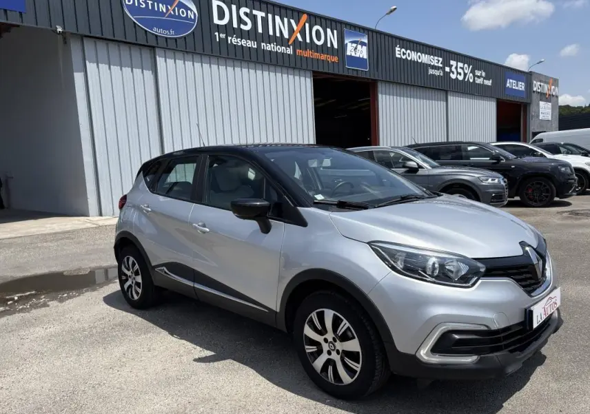 Renault Captur gris clair vue 3/4 avant droit, toit noir, jantes aluminium, stationné devant un garage multimarque.
