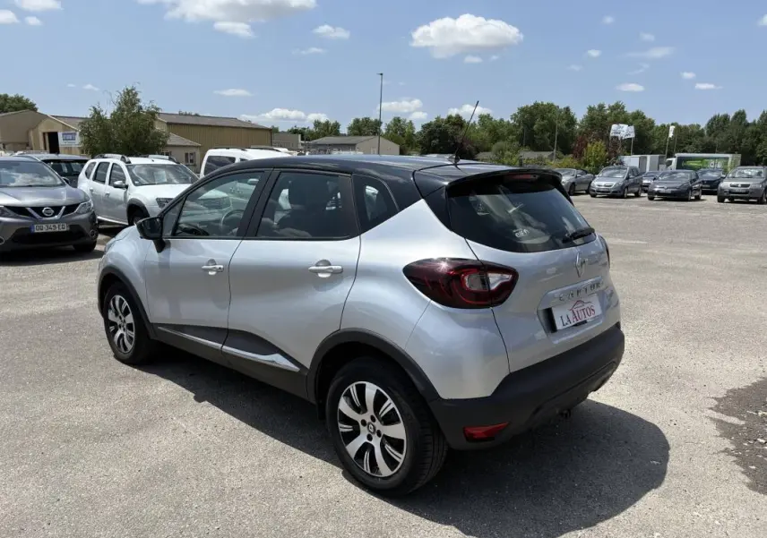 Vue 3/4 arrière droite d'un Renault Captur gris avec toit noir, jantes aluminium et vitres surteintées, stationné en extérieur.