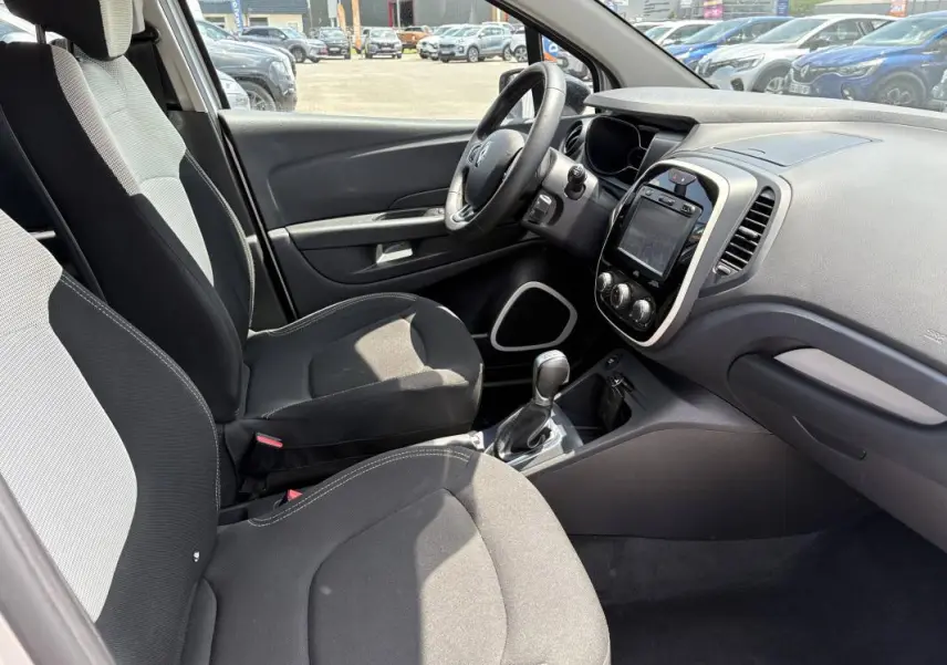 Vue intérieure côté conducteur du Renault Captur gris, montrant sièges tissu bicolore et tableau de bord avec écran tactile.