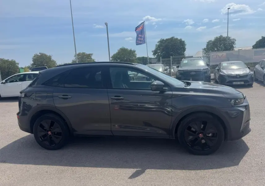 Profil côté gauche du DS7 hybride rechargeable gris foncé 2024 avec jantes alliage noires et barres de toit visibles.