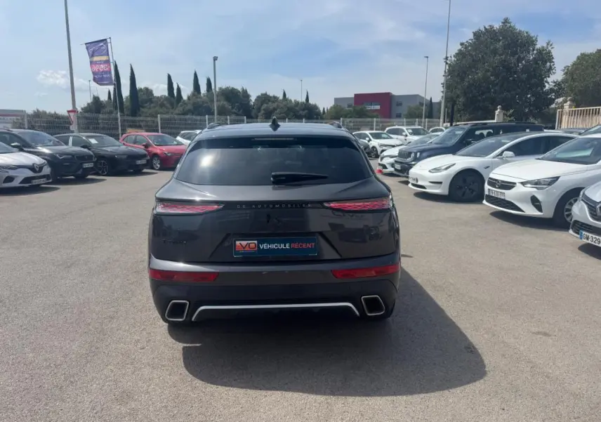 Vue arrière d'un DS7 gris foncé 2024 avec feux LED étirés, double sortie d'échappement et barres de toit visibles.