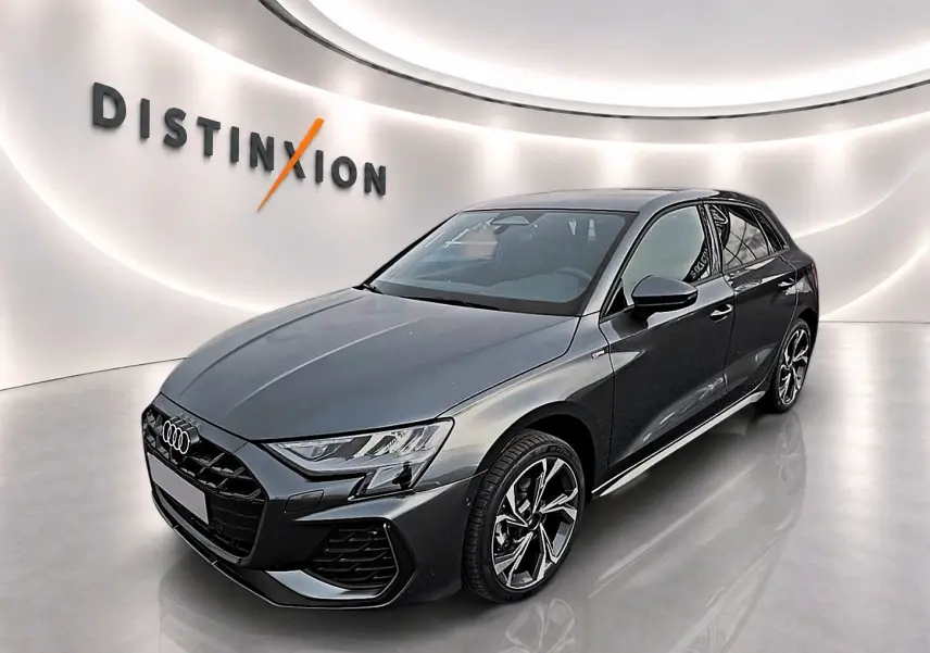 Audi A3 Sportback gris Daytona vue 3/4 avant droit dans un showroom lumineux avec logo Distinxion en arrière-plan.