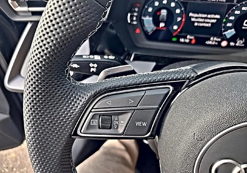 Gros plan sur le volant cuir perforé de l'Audi A3 Sportback 2026 avec commandes multifonctions et tableau de bord digital.