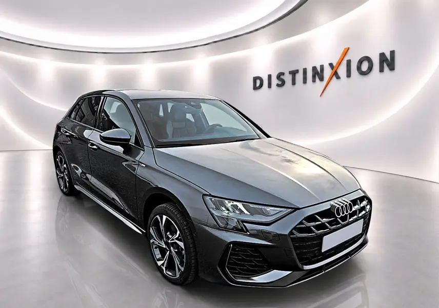 Audi A3 Sportback gris Daytona vue 3/4 avant droit dans un showroom lumineux avec logo Distinxion en arrière-plan.