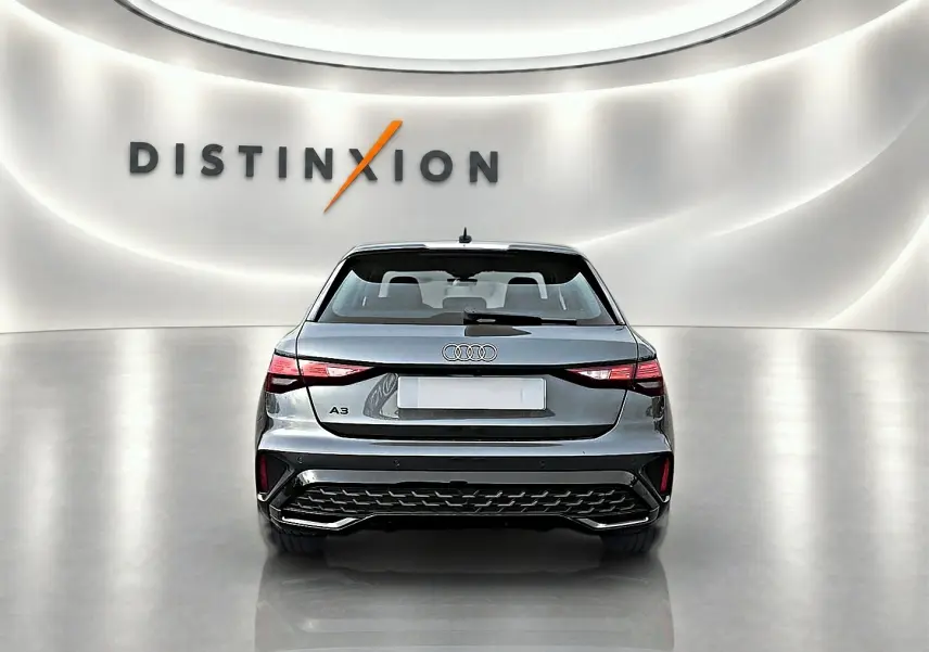 Vue arrière d'une Audi A3 Sportback gris Daytona avec feux LED et becquet arrière dans un showroom lumineux.