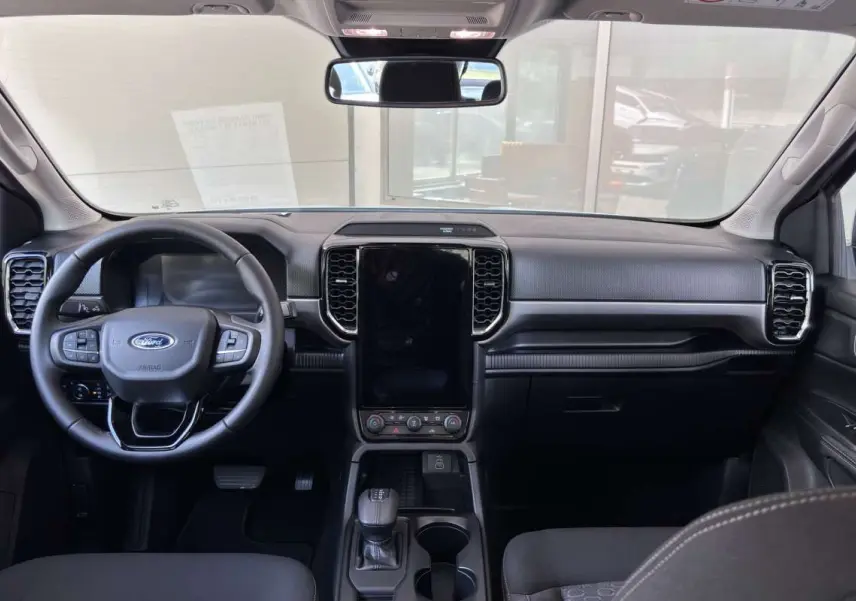 Vue intérieure avant du Ford Ranger 2.3 PHEV, tableau de bord noir avec écran tactile vertical et volant multifonctions.