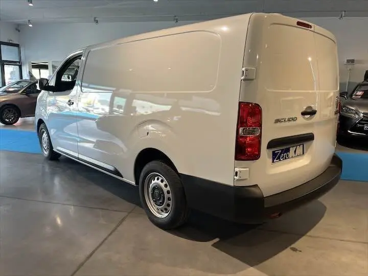 Vue 3/4 arrière droite d'un FIAT Scudo Fourgon blanc exposé en showroom avec plaque Zero KM visible.