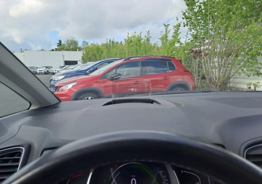 Vue depuis l'intérieur d'un Renault Scenic IV gris platine toit noir, avec tableau de bord et pare-brise visibles.