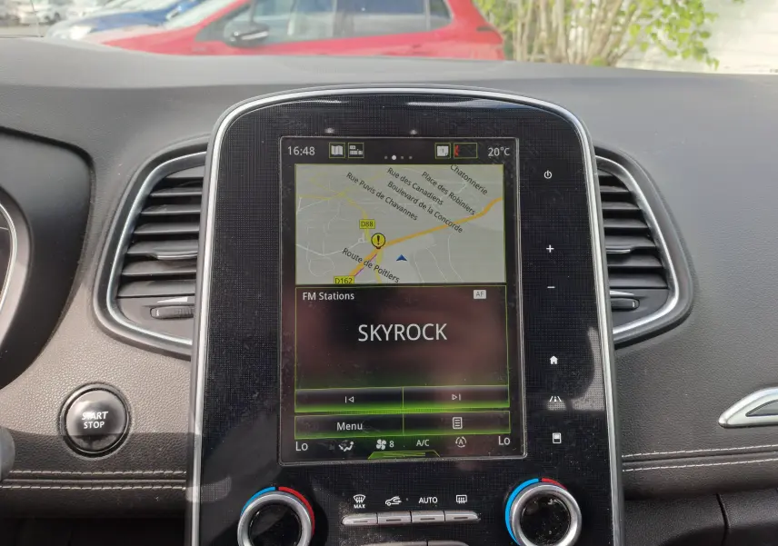 Vue rapprochée de l'écran central tactile du tableau de bord du Renault Scenic IV gris platine, affichant la radio Skyrock et la navigation.