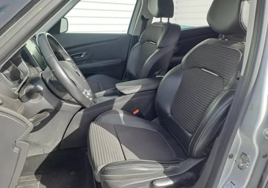 Vue intérieure côté conducteur du Renault Scénic IV 1.3 TCE 140 Intens avec sièges noirs en cuir et tissu, volant cuir et accoudoir central.