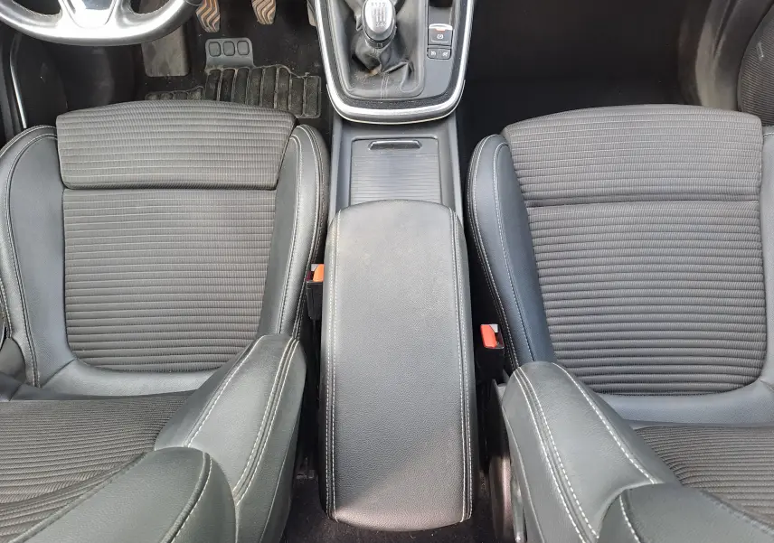 Vue plongeante sur les sièges avant en tissu noir et cuir, avec la console centrale et levier de vitesse manuelle d'un Renault Scenic IV gris platine.