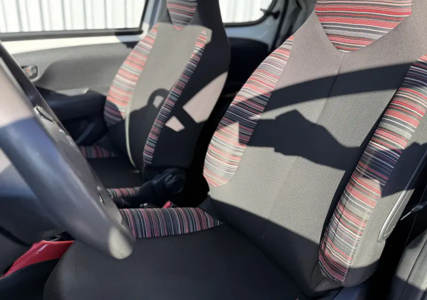 Vue intérieure rapprochée des sièges avant en tissu noir avec motifs rayés rouges et gris de la Citroën C1 blanche.