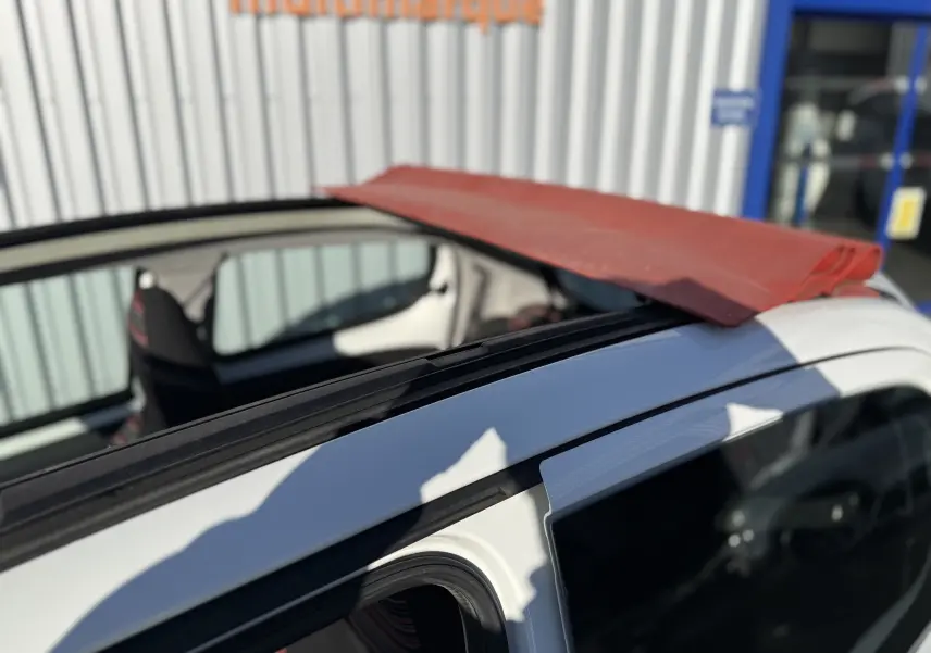 Toit ouvrant en toile rouge déployé sur une Citroën C1 blanche vue de côté droit, intérieur partiellement visible.