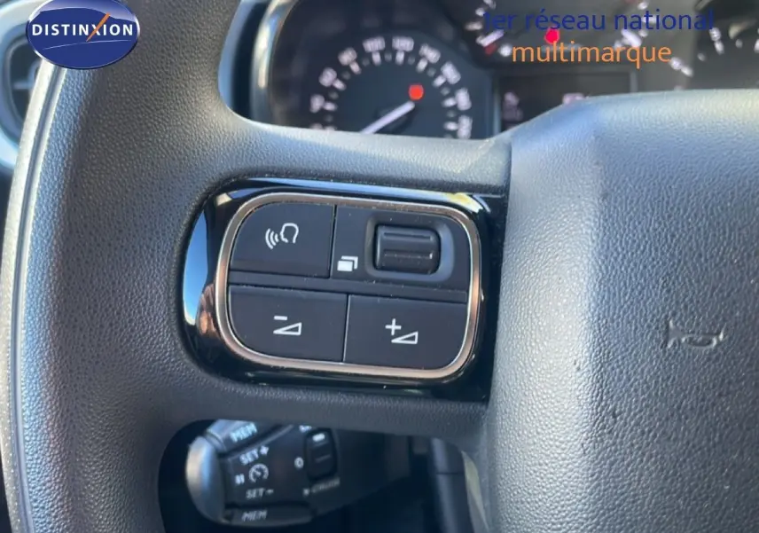 Gros plan sur les commandes au volant à gauche du Citroën C3 2020, intérieur noir avec tableau de bord flou en arrière-plan.